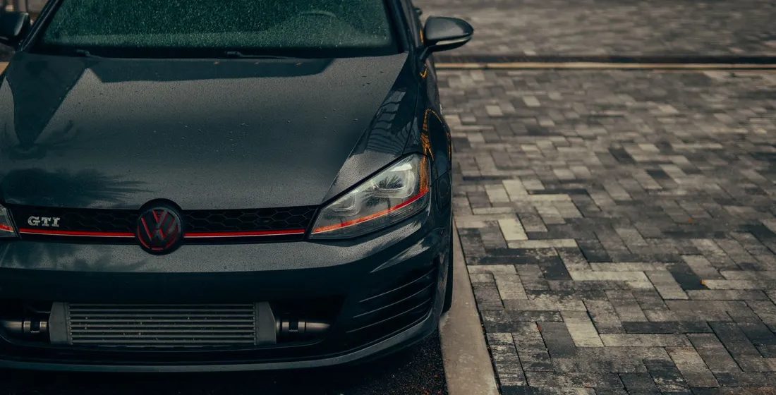 Volkswagen Golf GTI rouge garée sur un parking, face avant sportive et jantes alliage visibles.